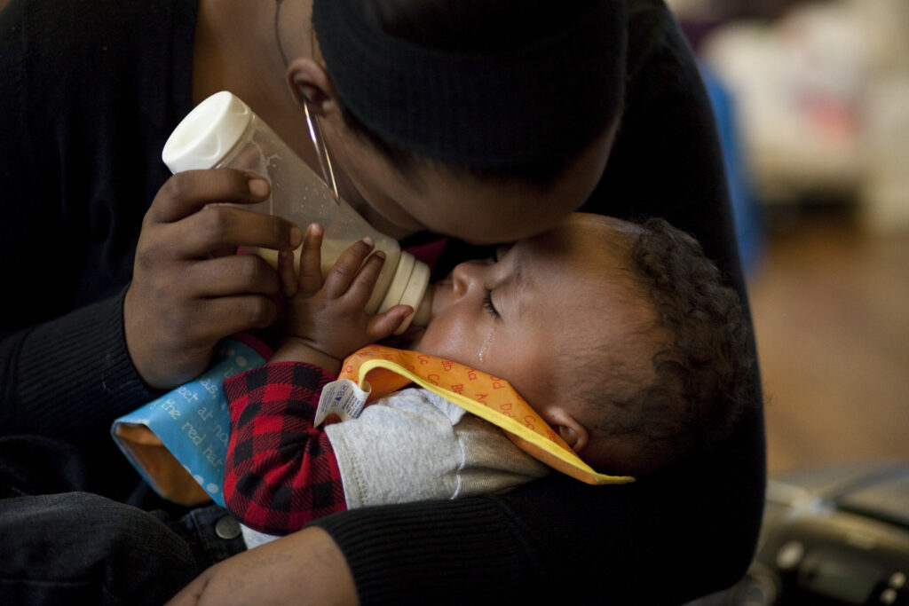 Black mom holding her baby and feeding baby a bottle of milk