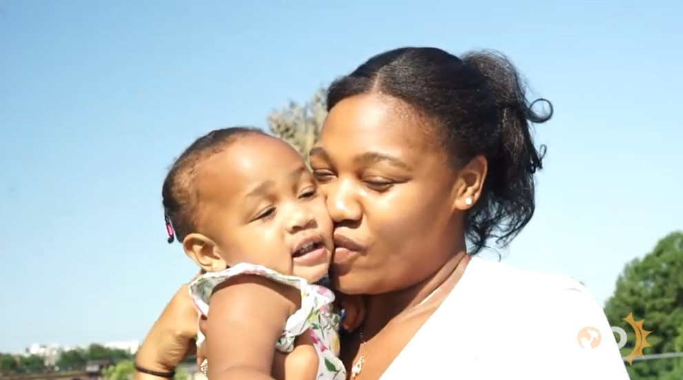 A Black mom holding and kissing her baby girl on the cheek outside